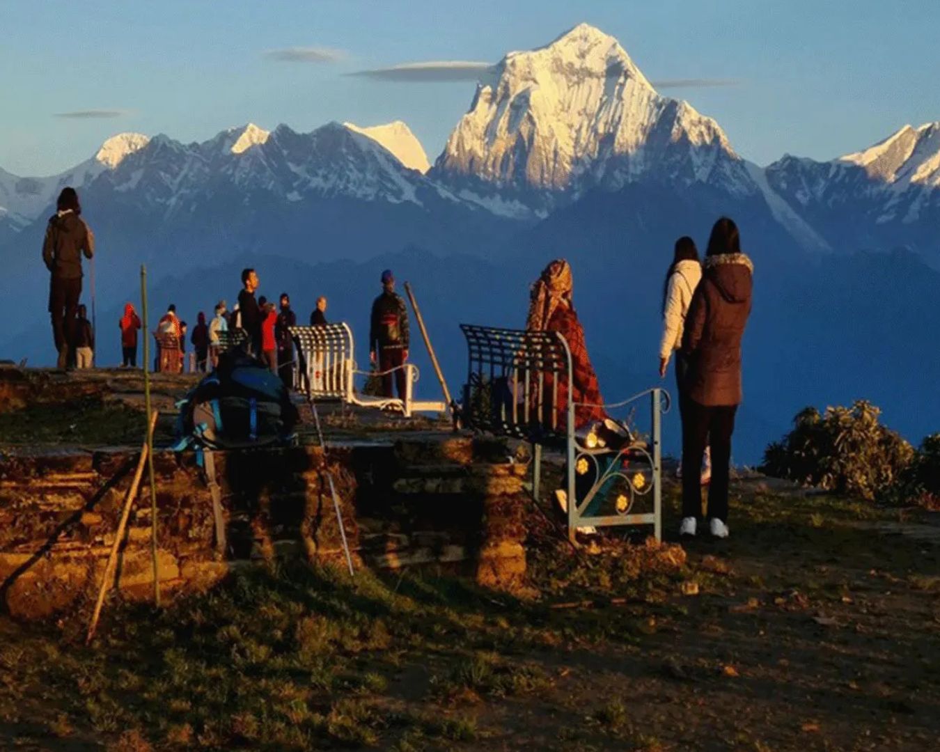 Film crew with equipment filming at sunrise in the Himalayas, with snow peaks in background