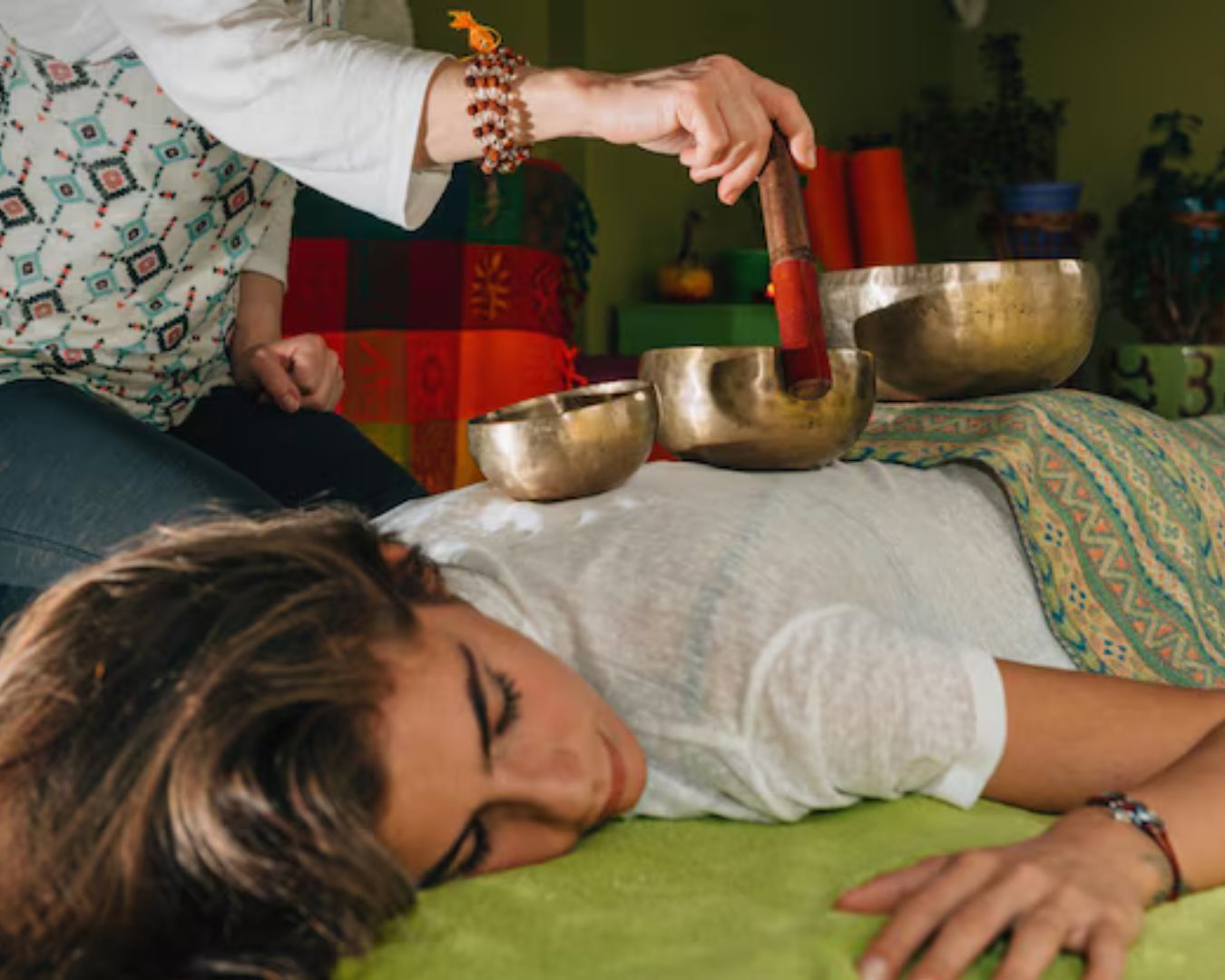 Sound therapy practitioner providing a singing bowl healing session on a relaxed client lying on a yoga mat.