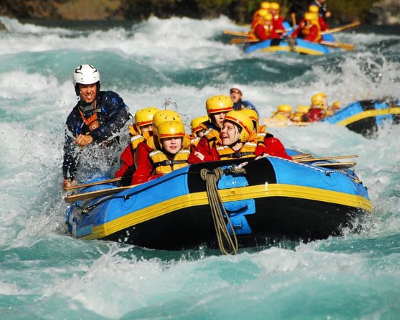 A group of people white-water rafting the rafting fast-flowing river of Nepal wearing a helmet and life jackets in a blue inflatable raft.